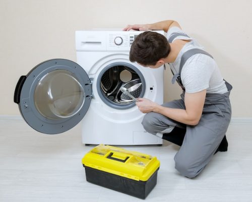 serviceman-repairs-broken-washing-machine-near-beige-wall_255755-4906